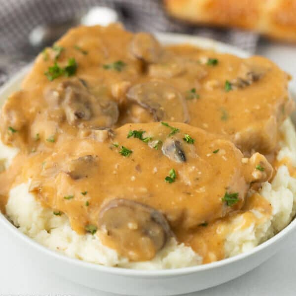 A bowl of mashed potatoes topped with creamy brown mushroom gravy and garnished with chopped parsley, just like the comforting flavors in a crock pot smothered pork chops recipe.