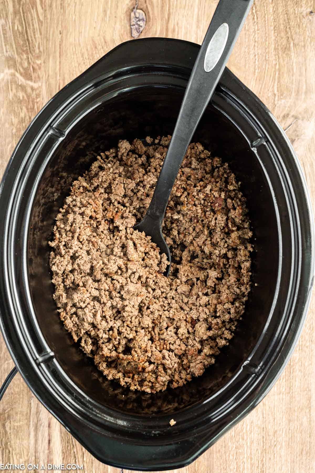 Placing ground beef in the slow cooker with a spoon
