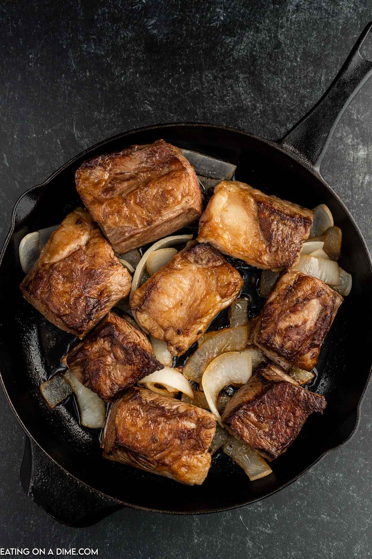 cooked short ribs in the skillet with onions