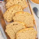 Sliced loaf of homemade peanut butter bread on a wooden cutting board, with a butter knife and a jar of peanut butter nearby on a light surface.