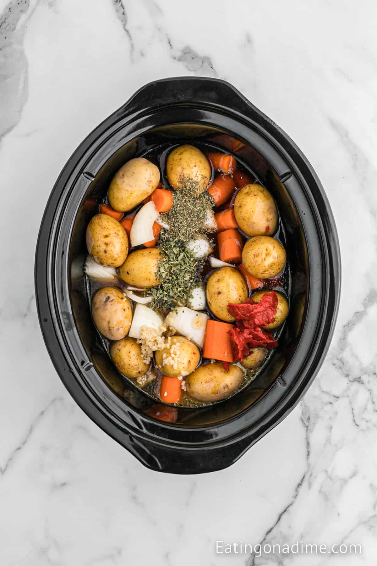 Roast in the slow cooker topped with potatoes, carrots, and onions topped with seasoning