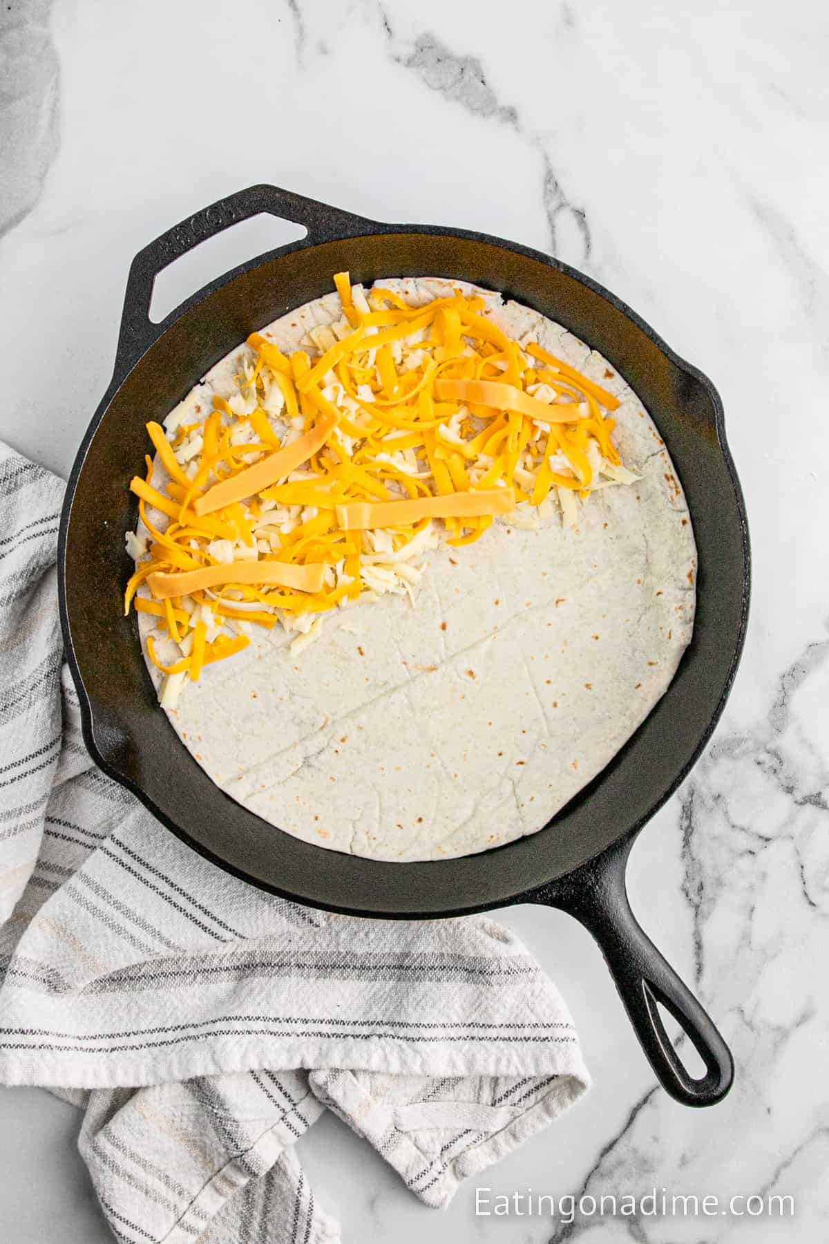 Flour tortilla in cast iron skillet topped with shredded cheese
