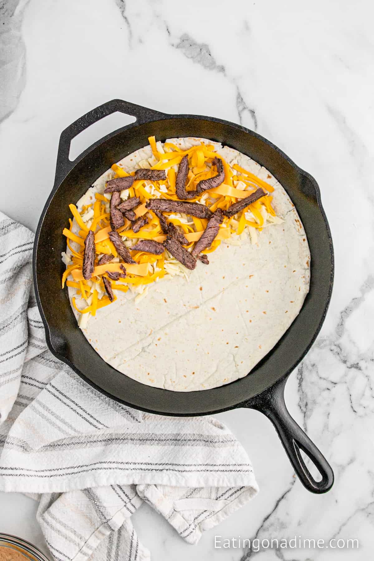 Flour tortilla in cast iron skillet topped with shredded cheese and steak strips