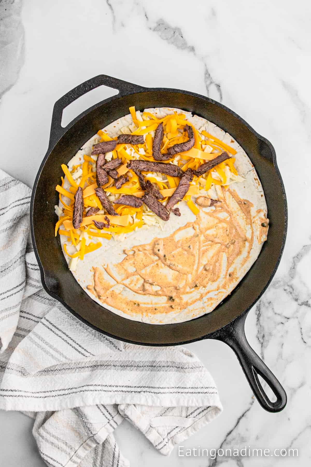 Spreading sauce on the tortilla and topped with shredded cheese and steak strips