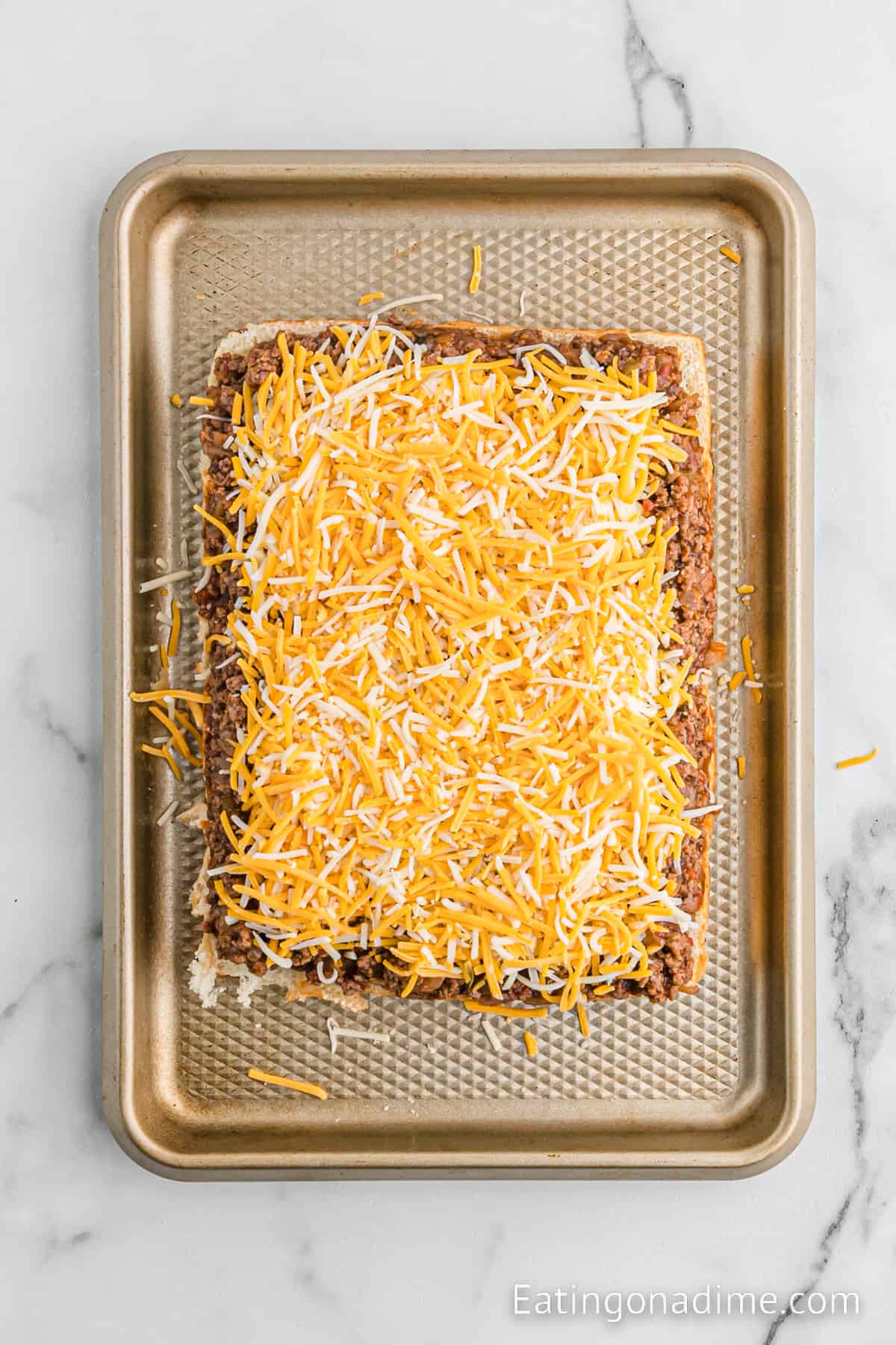 Bottom of Hawaiian Rolls topped with cooked ground beef and shredded cheese