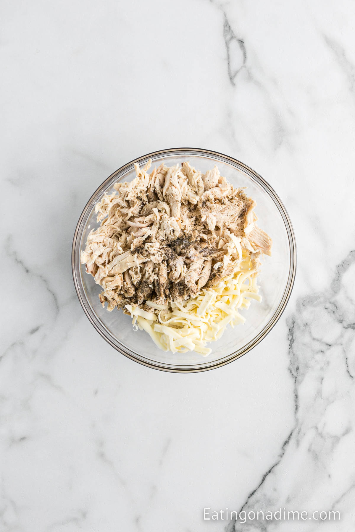 Shredded chicken in a bowl with shredded cheese and seasoning