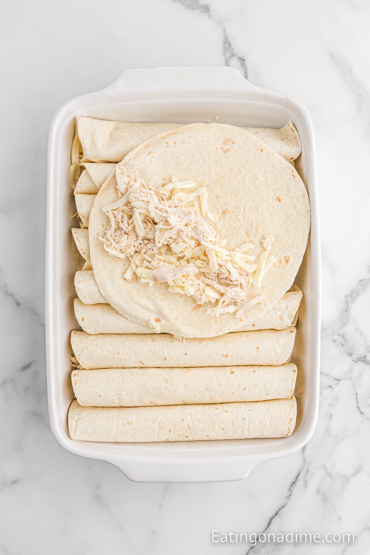Flour tortillas rolled up with shredded chicken in the center in a baking dish