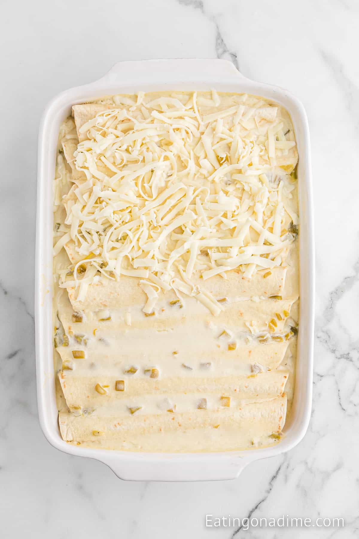 Enchiladas in a baking dish topped with a creamy sauce and shredded cheese