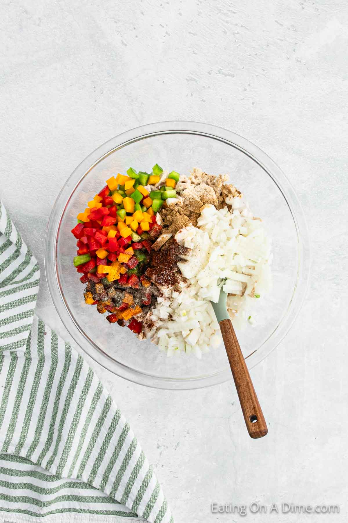 Combining the cooked chicken, salsa, seasoning, peppers, and onions in a bowl with a wooden spoon