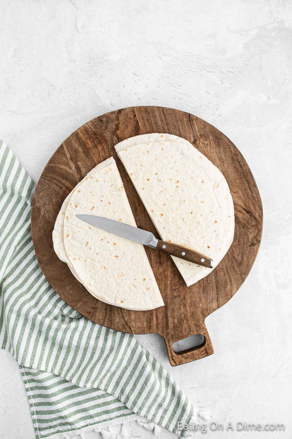 Cut tortillas in a half on a cutting board with a knife