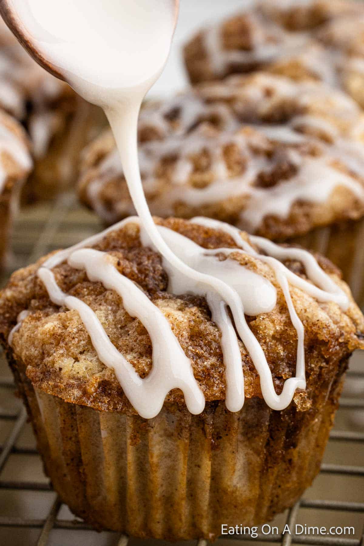 Cinnamon roll muffins on a wire rack being topped with a glaze
