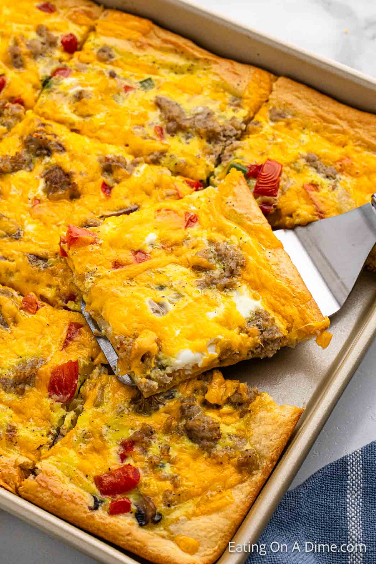 Crescent Roll Breakfast Pizza sliced on a baking sheet with a serving on a spatula