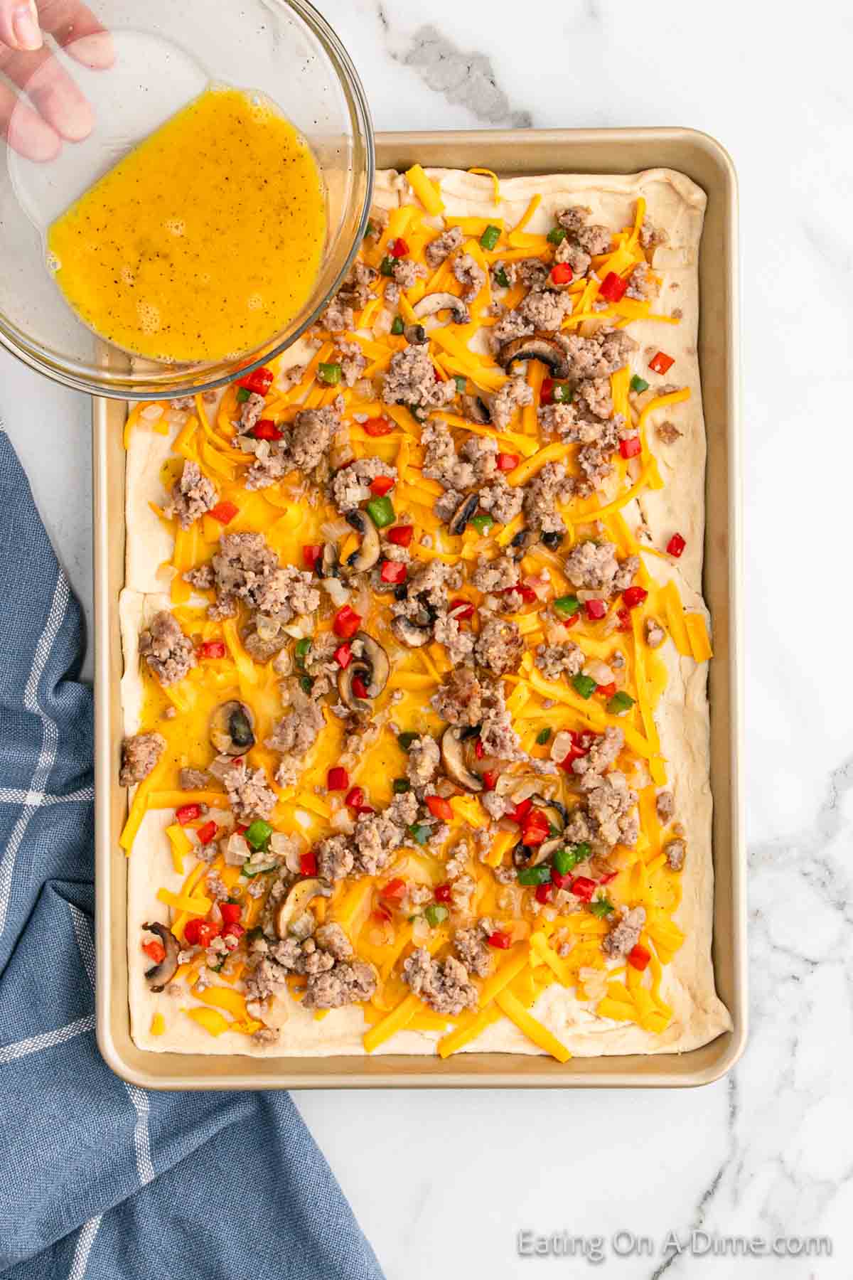 Pouring the egg mixture onto the baking sheet with the dough, veggies and sausage and cheese