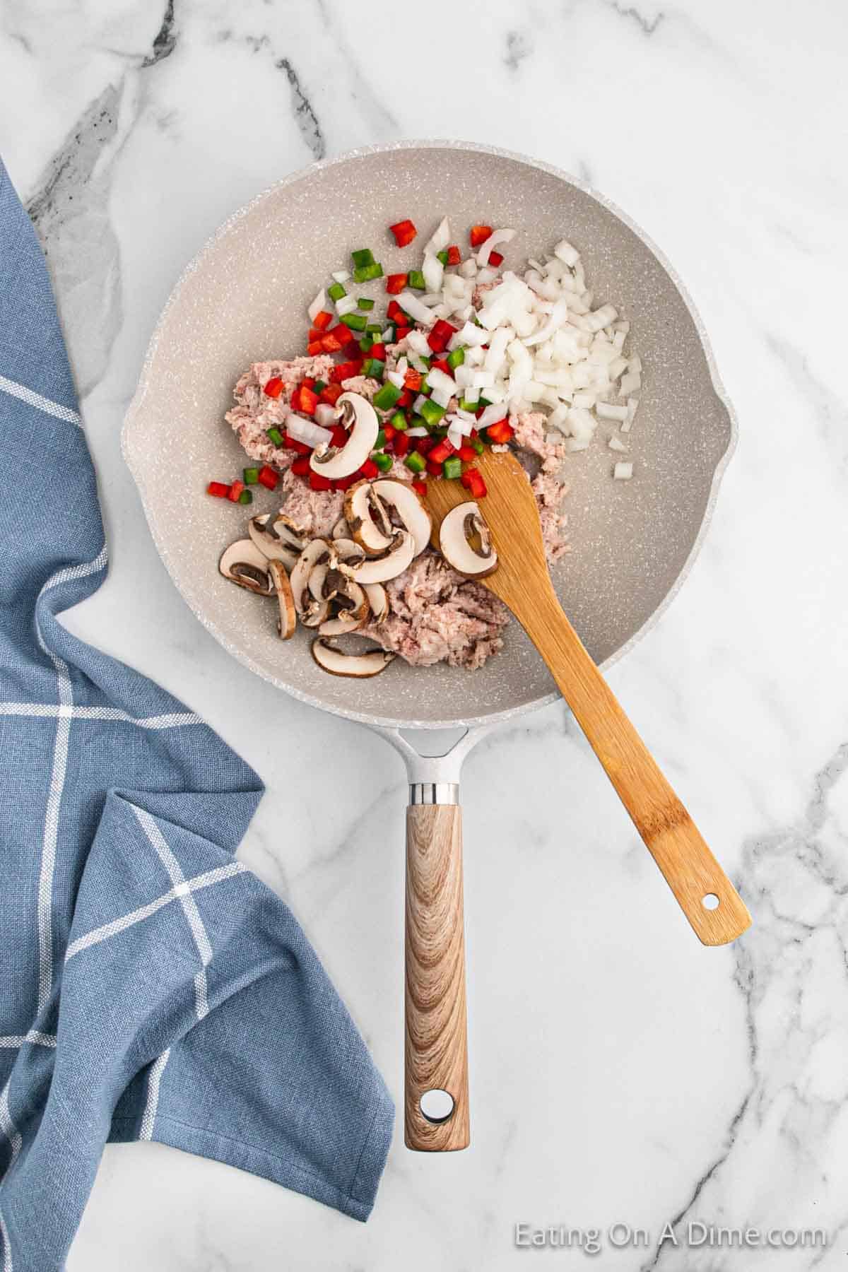 Cooking ground sausage, mushrooms, diced onions and bell peppers in a skillet with a wooden spoon