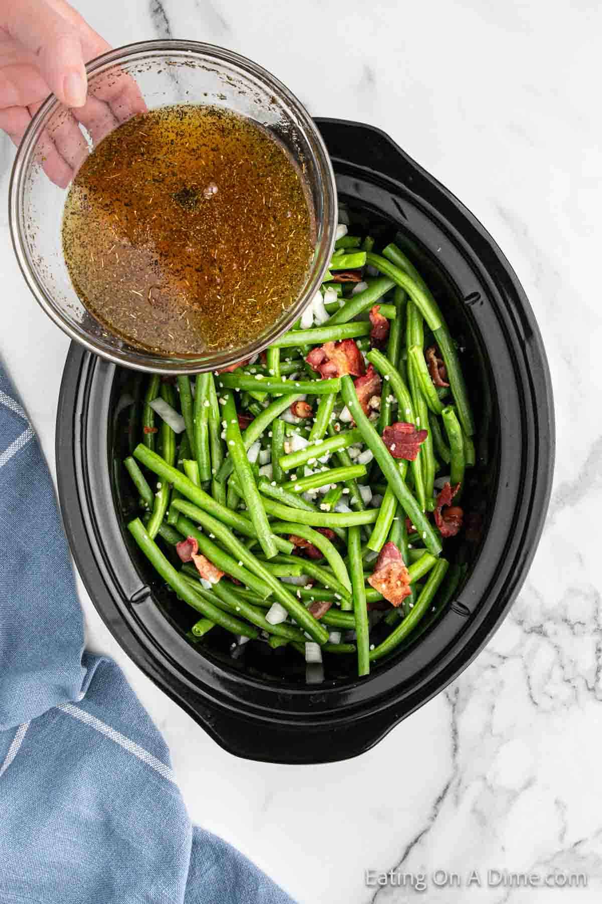 Pouring the broth mixture over the top of the fresh green bean mixture in the slow cooker