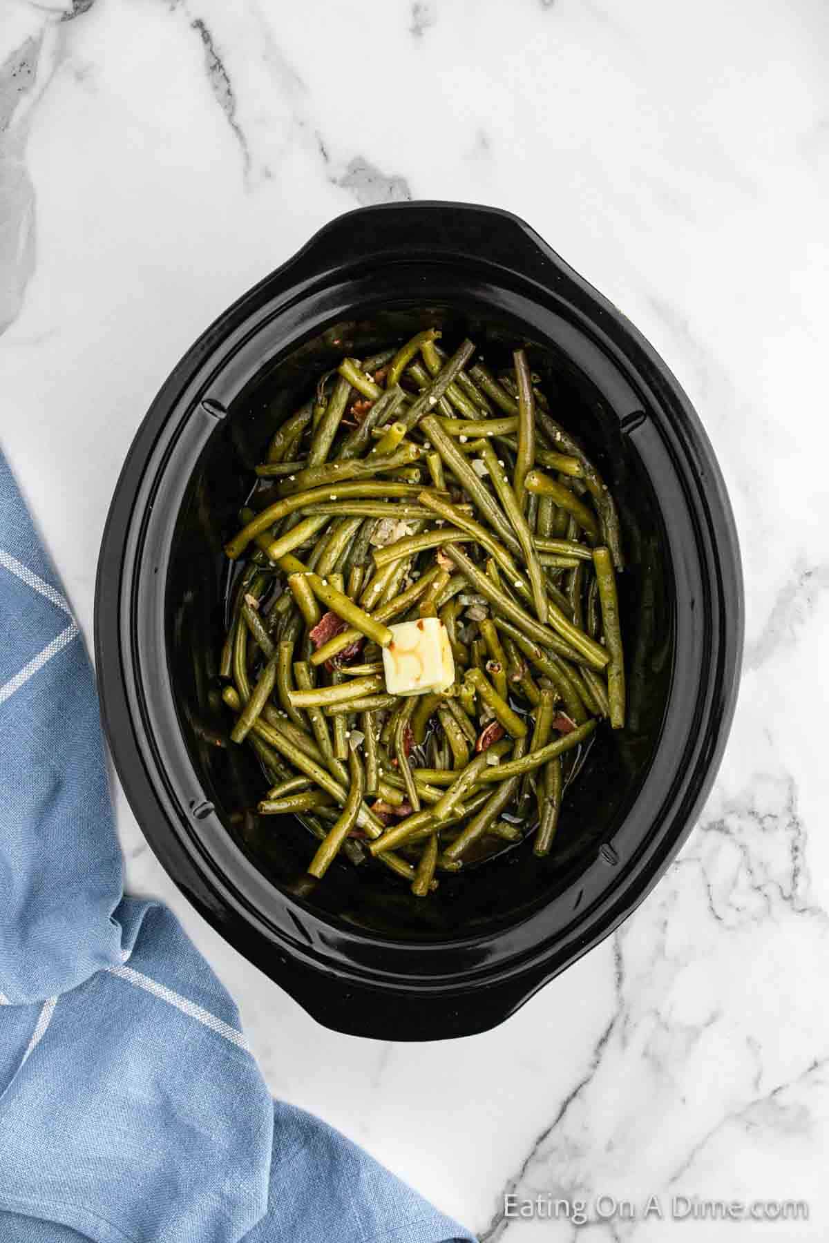 Cooked green beans in the slow cooker topped with slice of butter