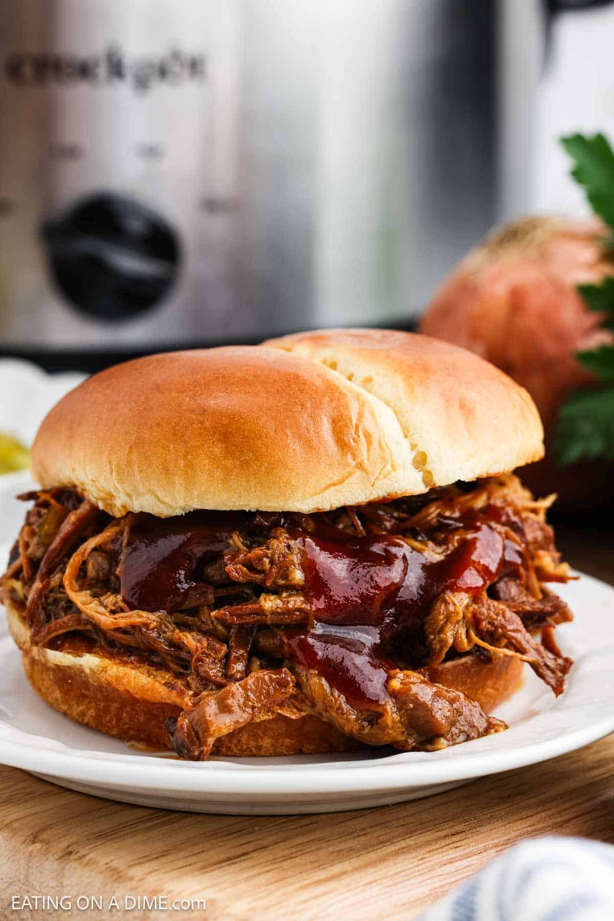 Shredded pork sandwich topped with BBQ sauce on a plate.