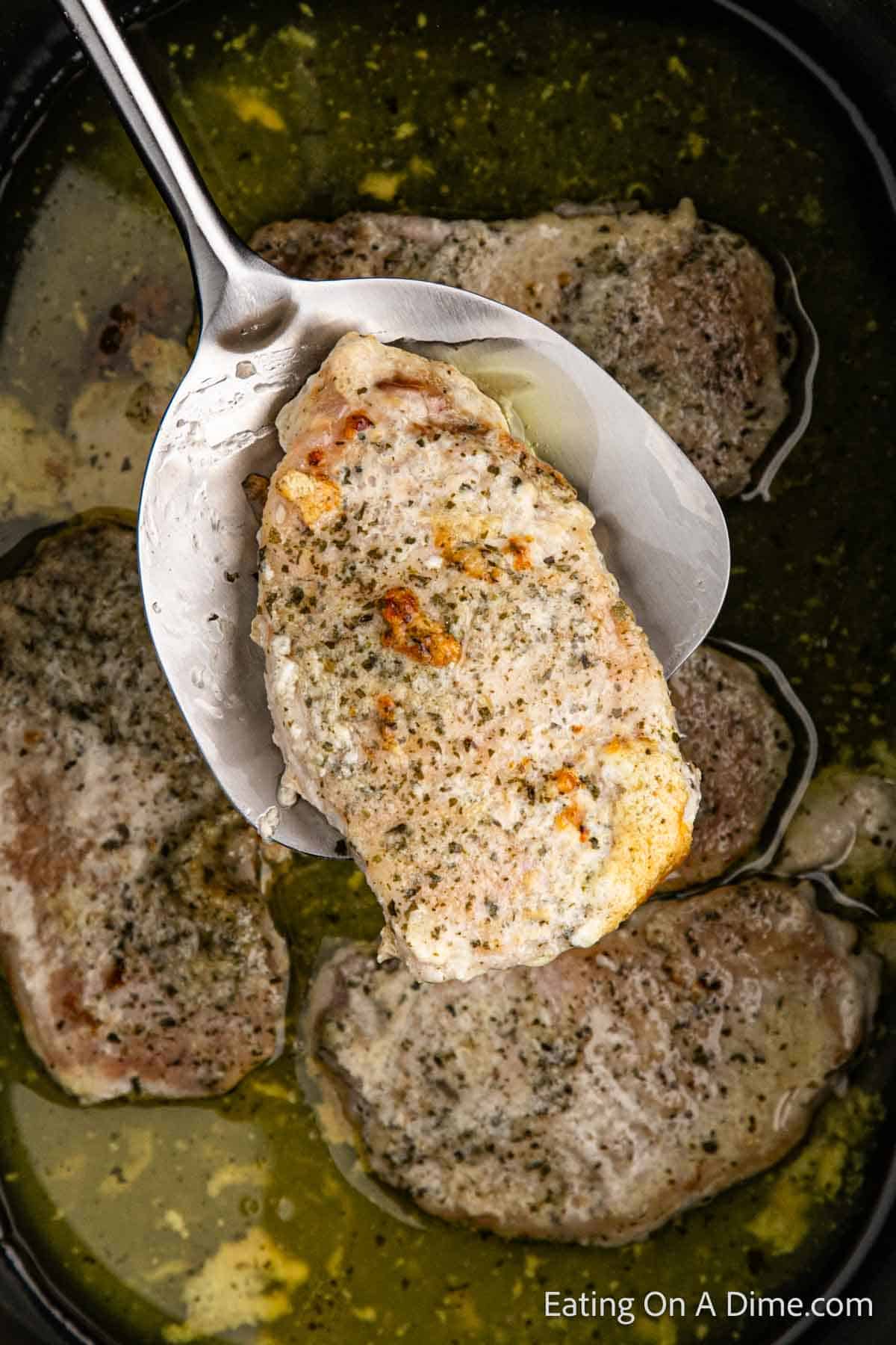 Cooked Ranch Pork Chops on a serving spoon and pork chops in the slow cooker