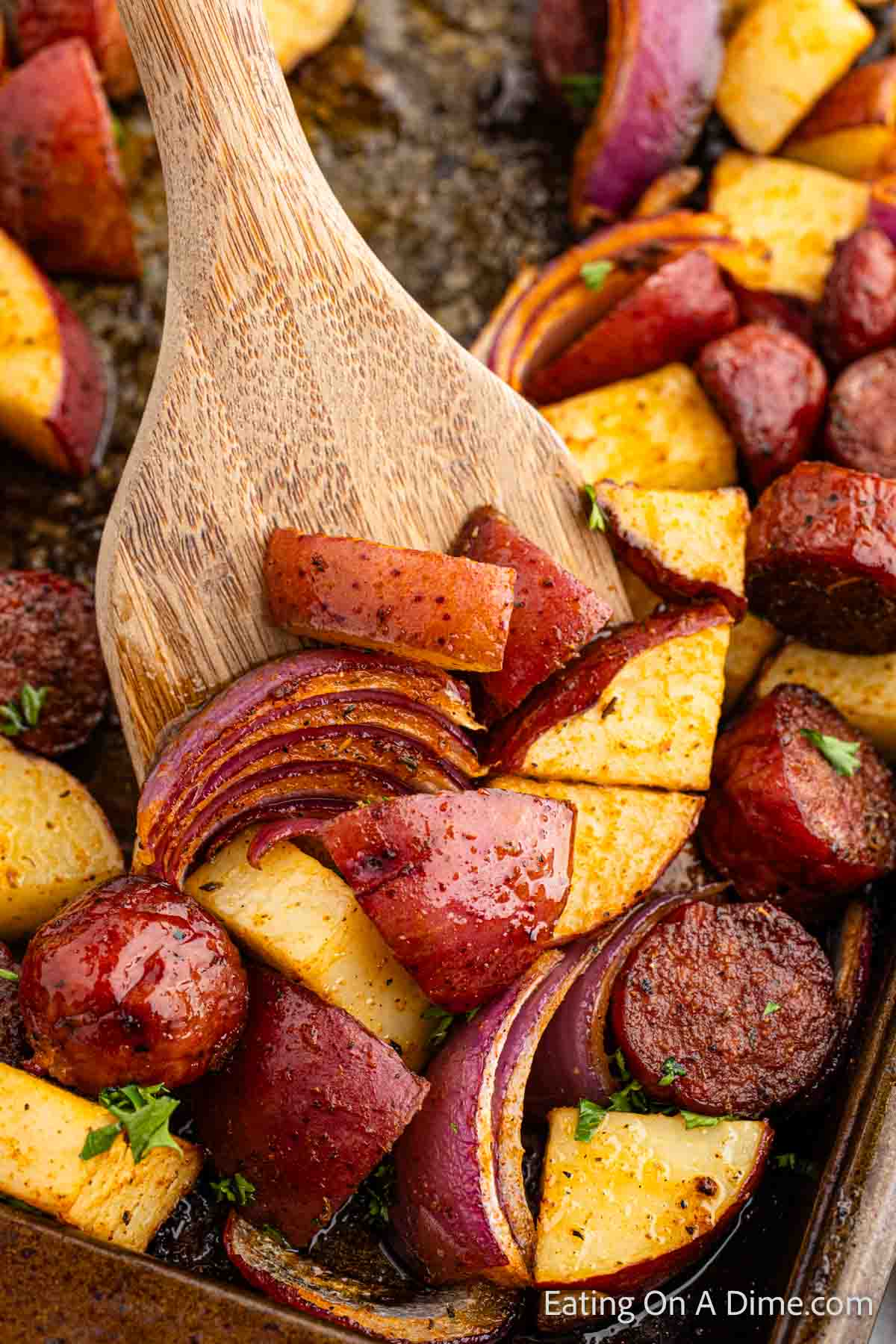 Close up image of roasted potatoes, onions and sausage with a serving on a wooden spoon