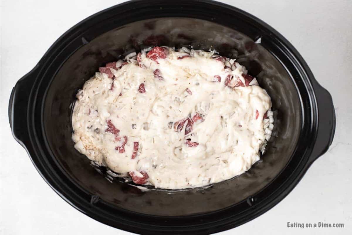 Topping the stew meat with the additional ingredients in the slow cooker