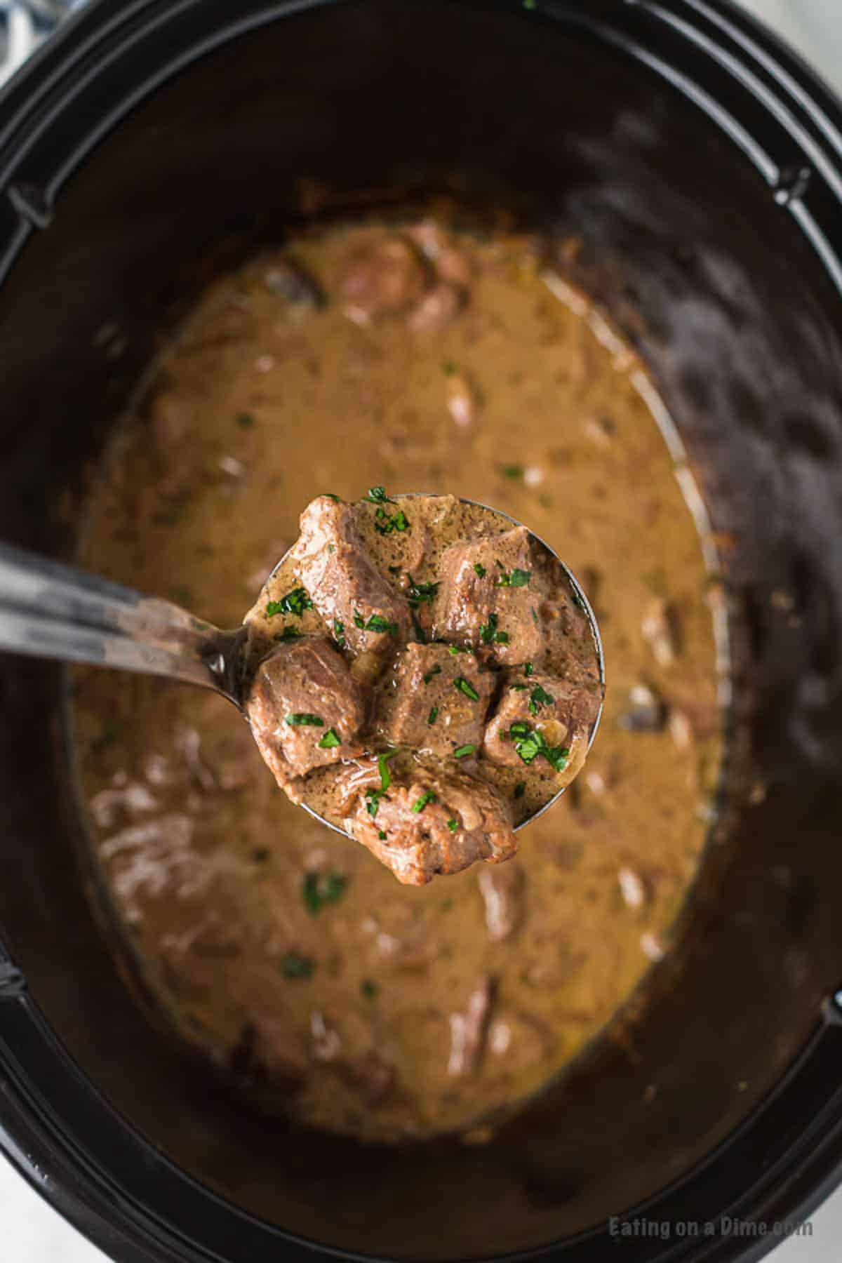 Beef Tips and gravy in the slow cooker with a serving on a ladle