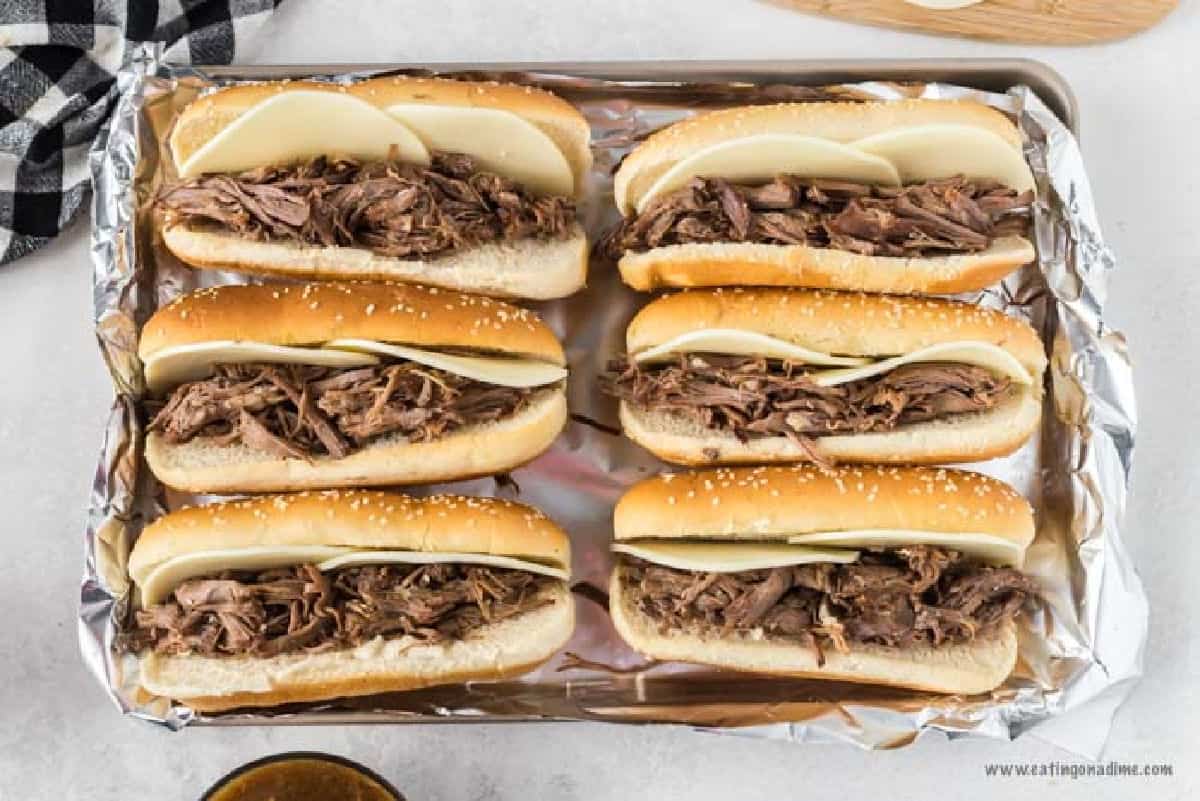 Placing the cooked shredded beef in the hoagies with cheese and placing on the baking sheet