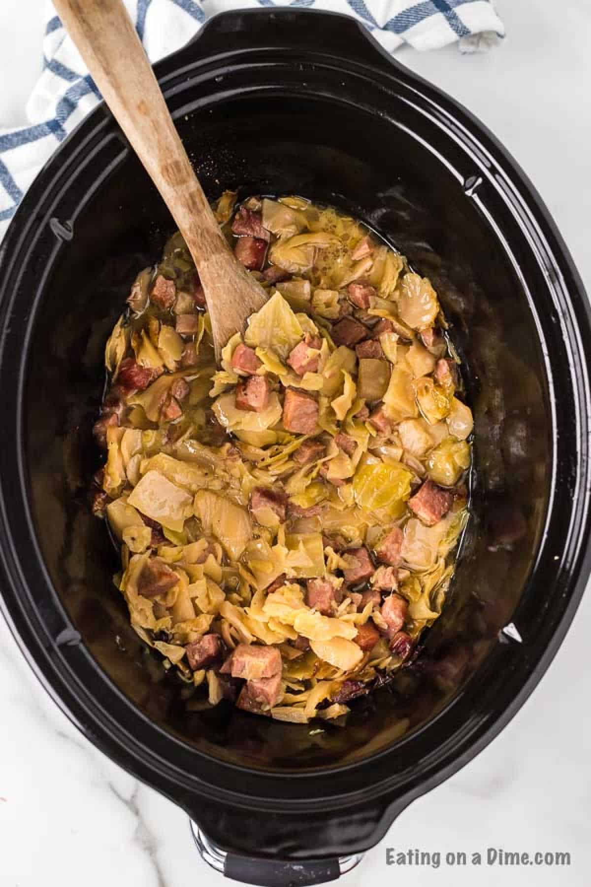 cabbage and ham in the slow cooker with a wooden spoon