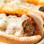 Close-up of a crockpot meatball sub on a sesame seed hoagie roll, topped with melted mozzarella cheese, marinara sauce, and garnished with chopped parsley.