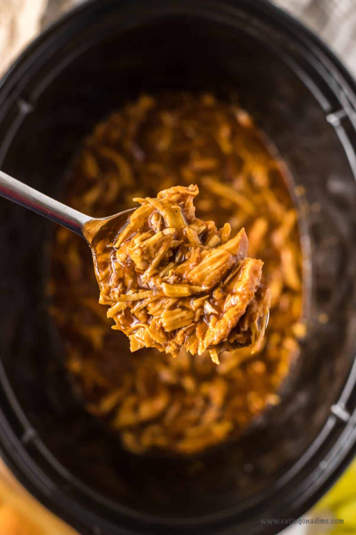 Close up image of shredded BBQ Chicken in the slow cooker and a serving on a spoon