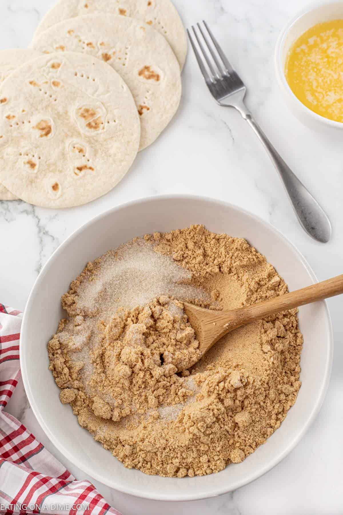 Graham cracker crumbs mixed with sugar in a bowl with a wooden spoon
