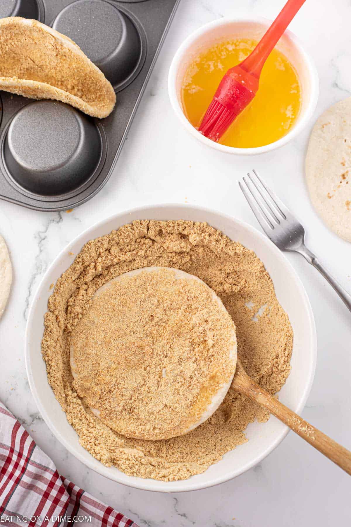 Flour tortilla being placed in a bowl then covered with the graham cracker mixture 