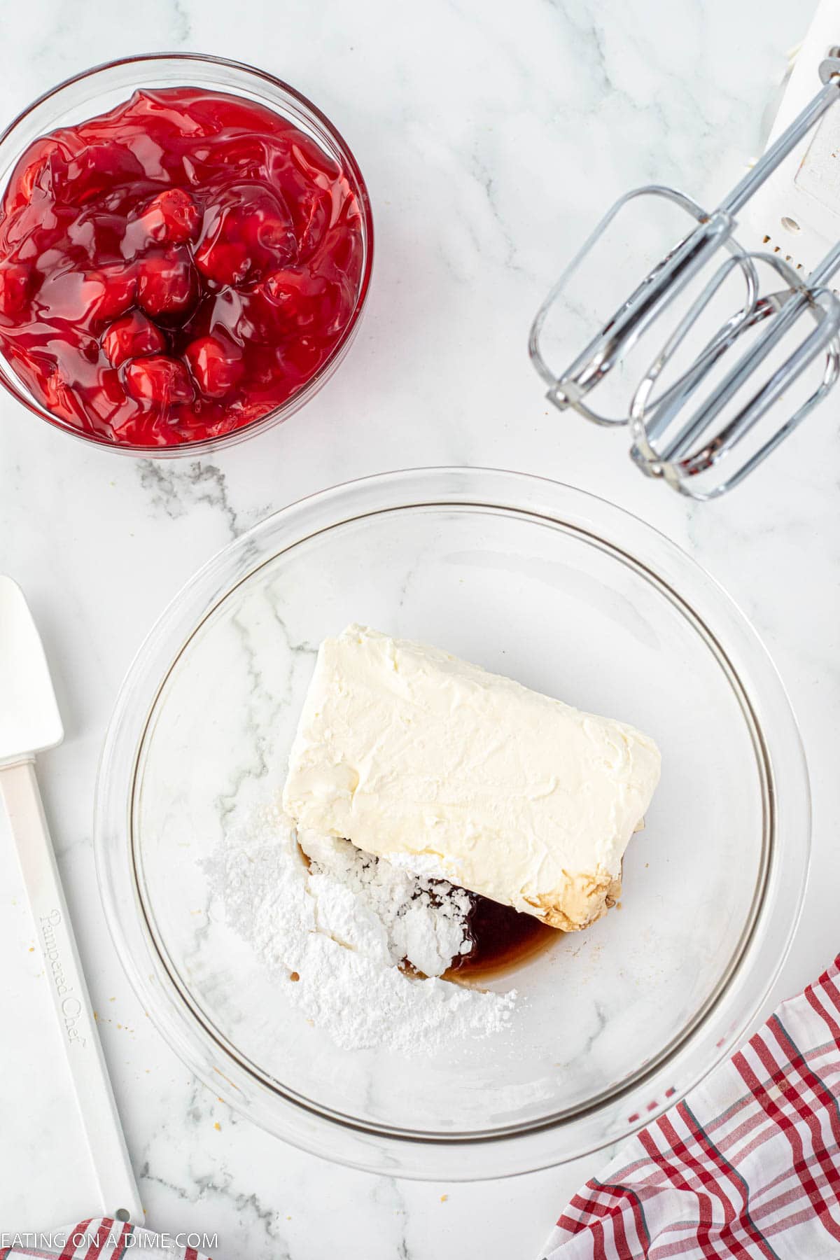Cream cheese in a bowl with powdered sugar and vanilla extract with a bowl of cherry pie filling on the side