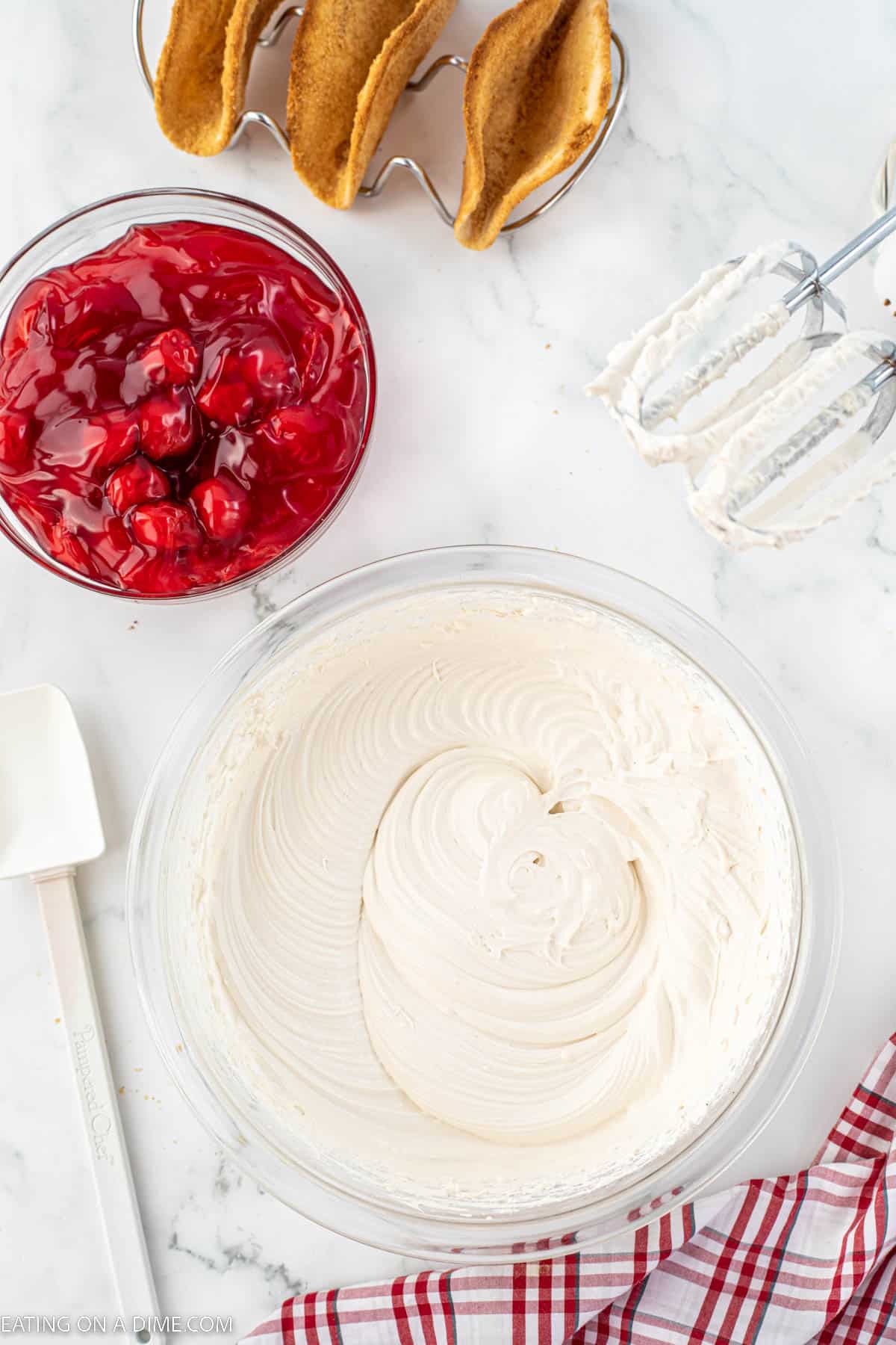 Whipped topping mixed with cream cheese mixture in a bowl with a bowl cherry pie filling on the side