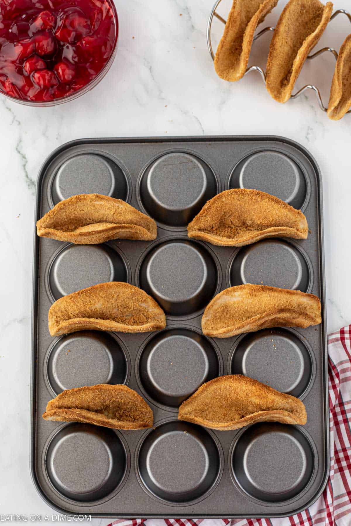 Turned over muffin pan topped with baked graham cracker covered tortillas 