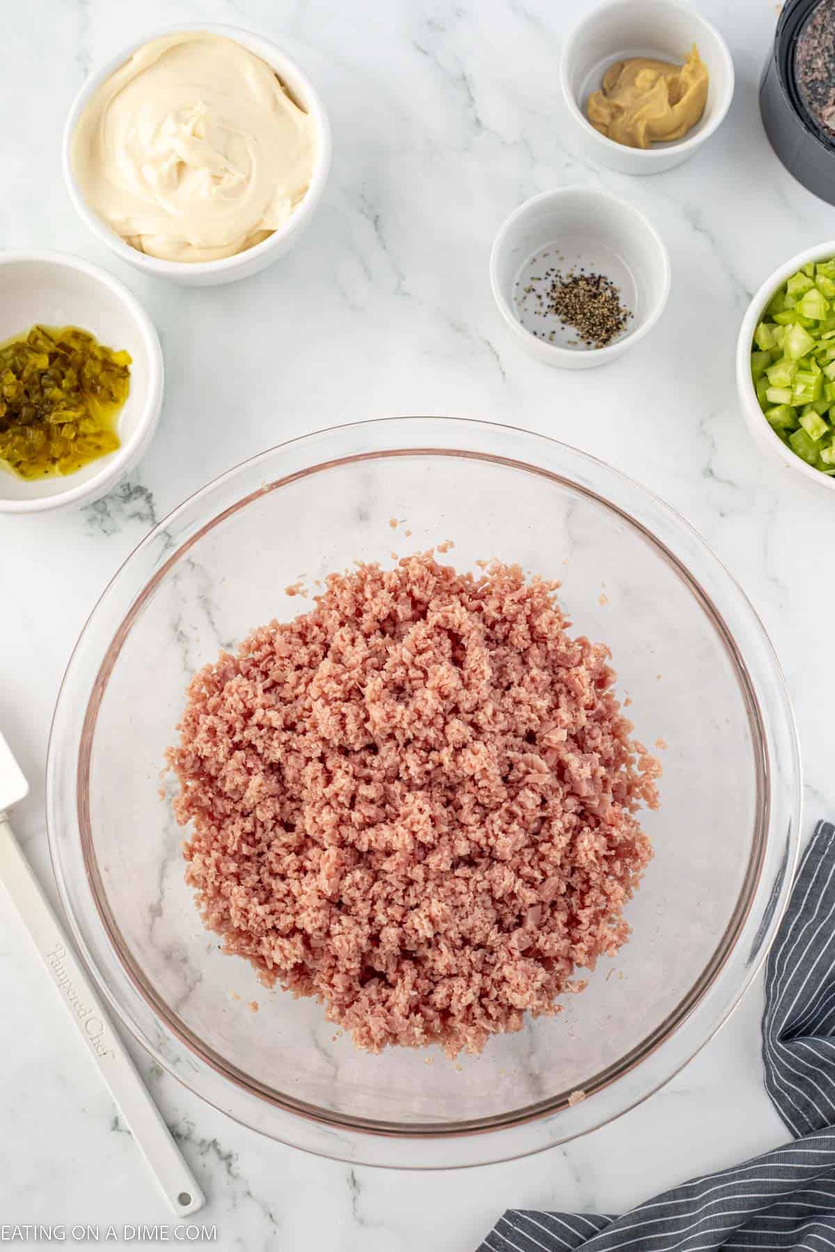 Ham diced in a bowl with a bowl of mayo, relish, pepper, mustard