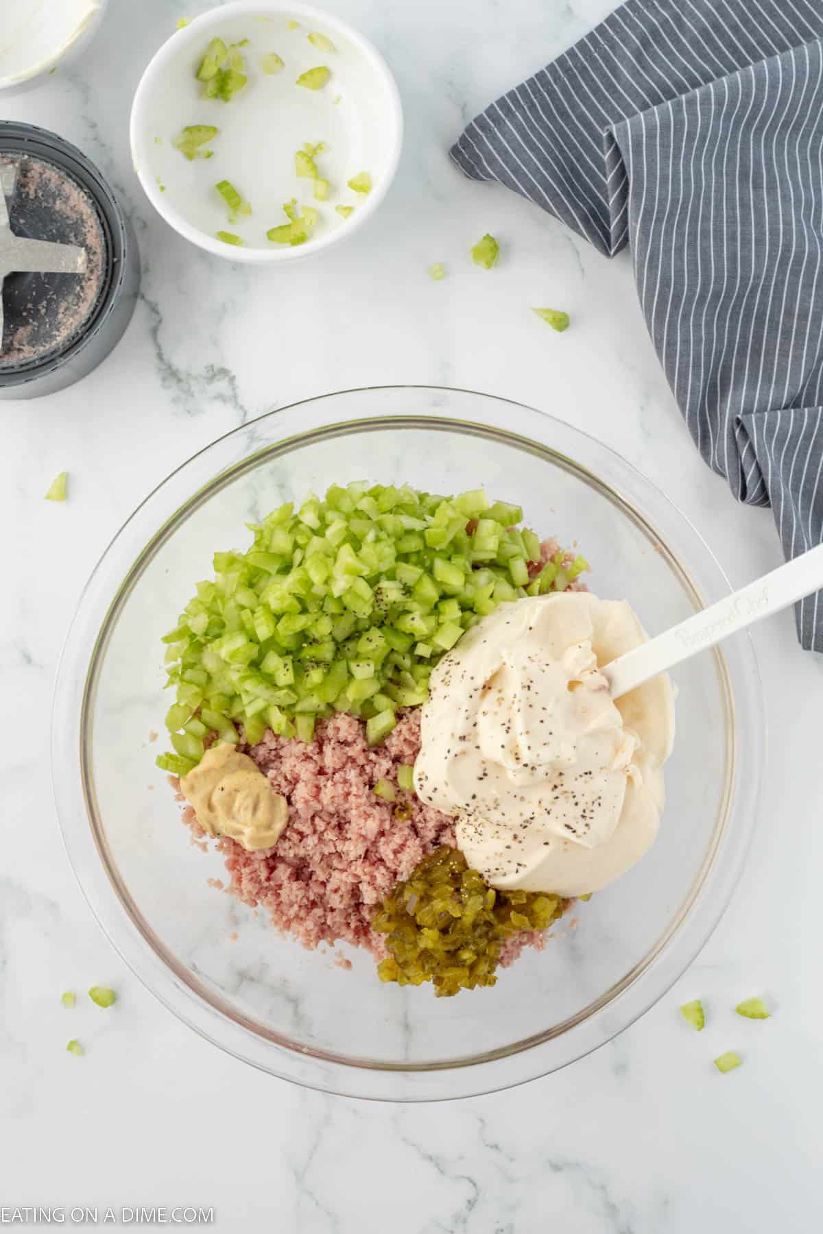 Adding in chopped celery, mayo, mustard, and relish in a bowl with a spatula