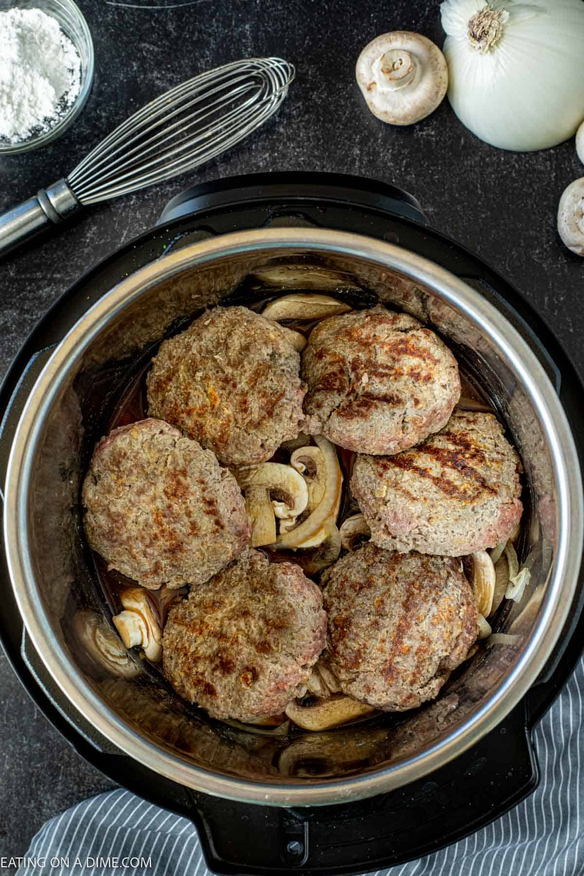 Placing mushrooms and onions in a pressure cooker topped with ground beef patties