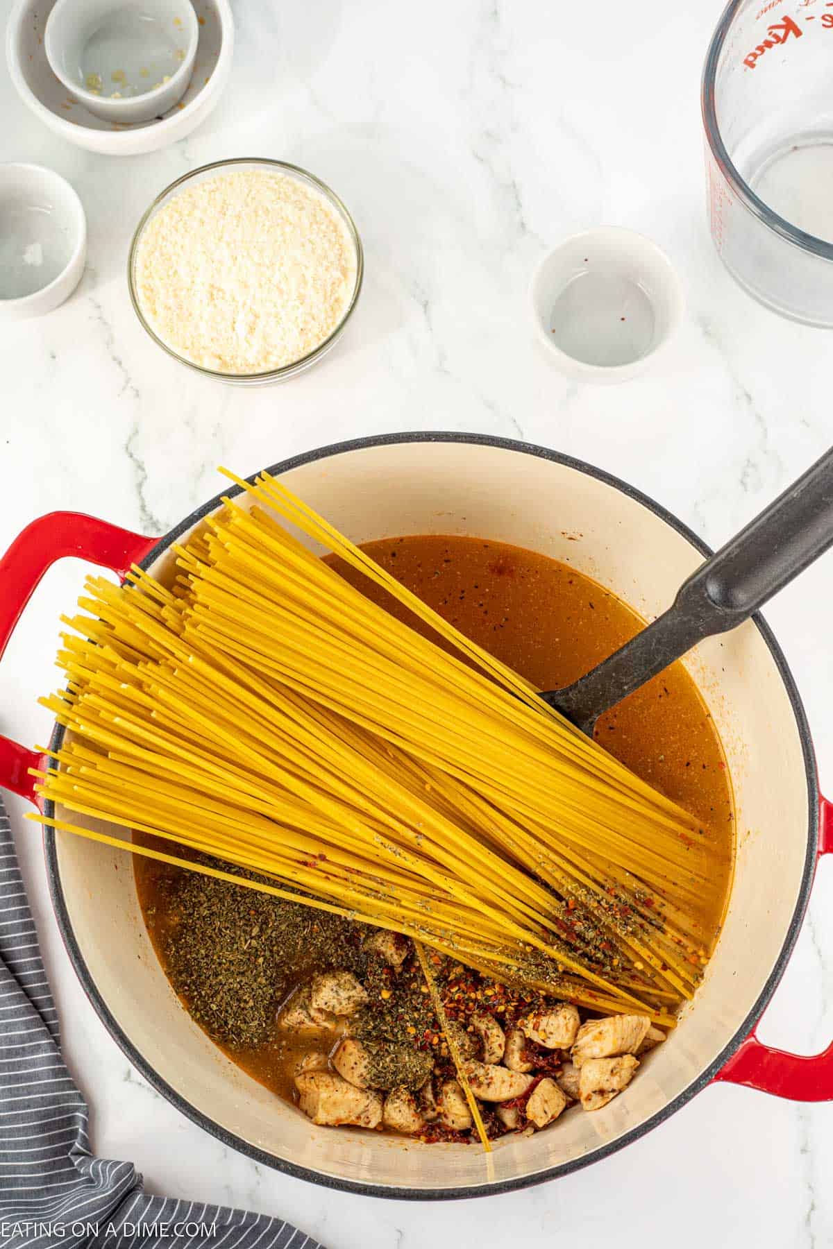 Large pot with spaghetti noodles in broth with cooked chicken and seasoning