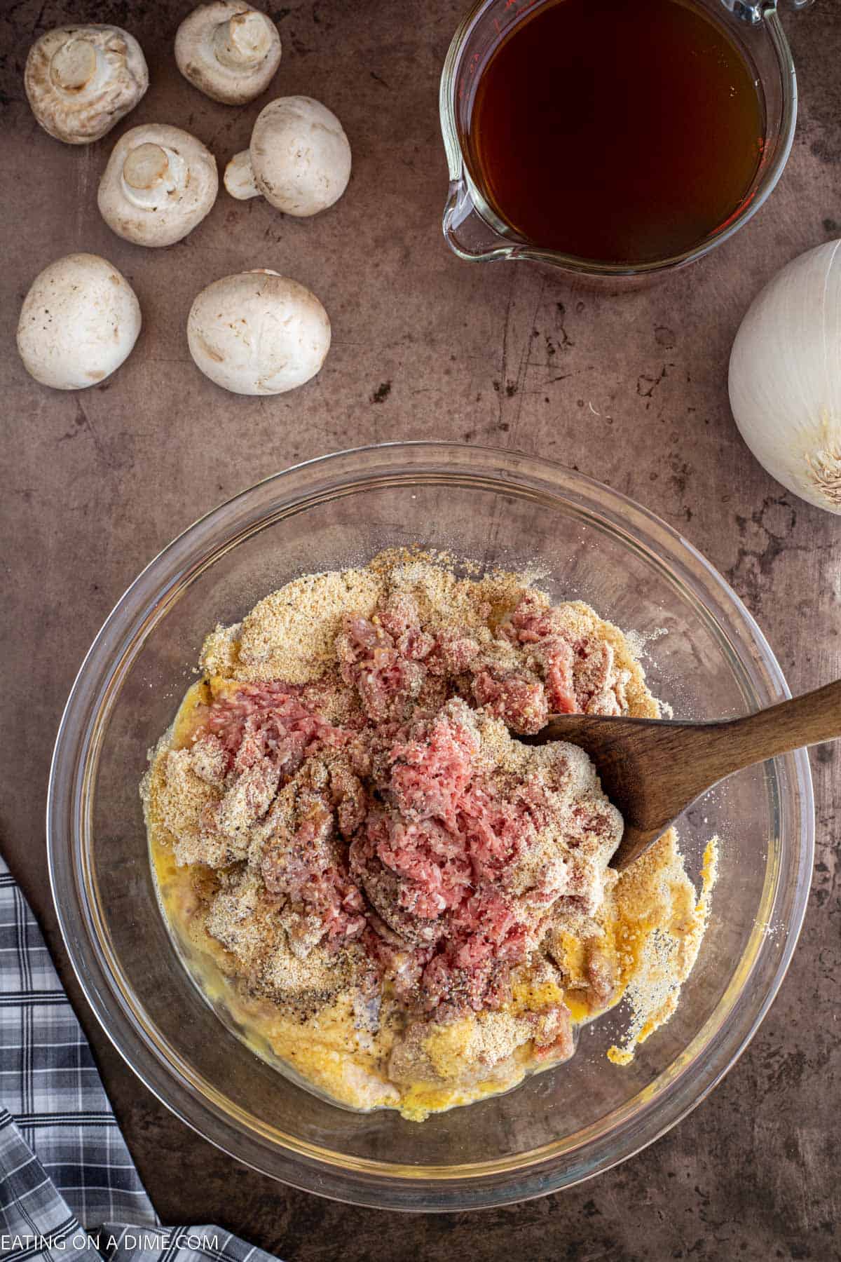 Combining ground beef with seasoning in a bowl with a wooden spoon