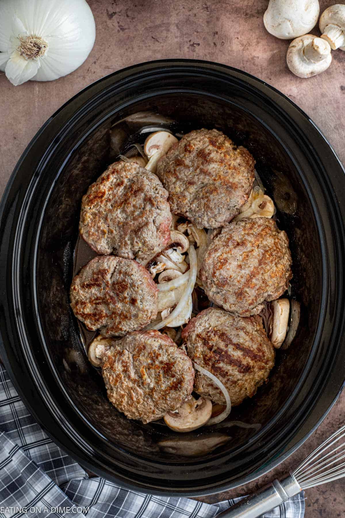 Placing the beef patties in teh slow cooker with the onions and mushrooms