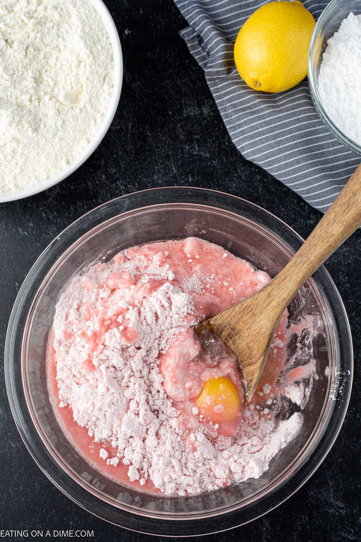 Combining strawberry cake mix with other ingredients in a bowl with a wooden spoon