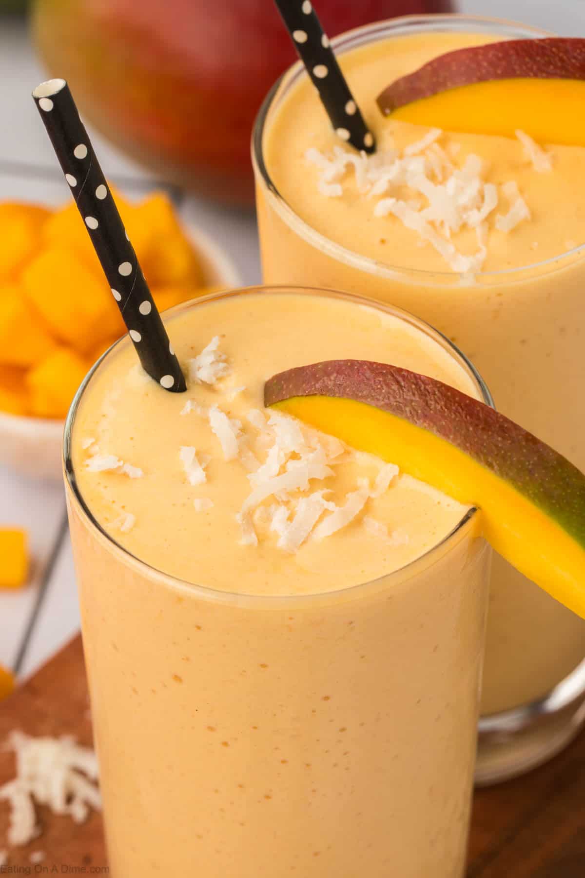 Mango Smoothies in a glass topped with shredded coconut and a slice of fresh mangos