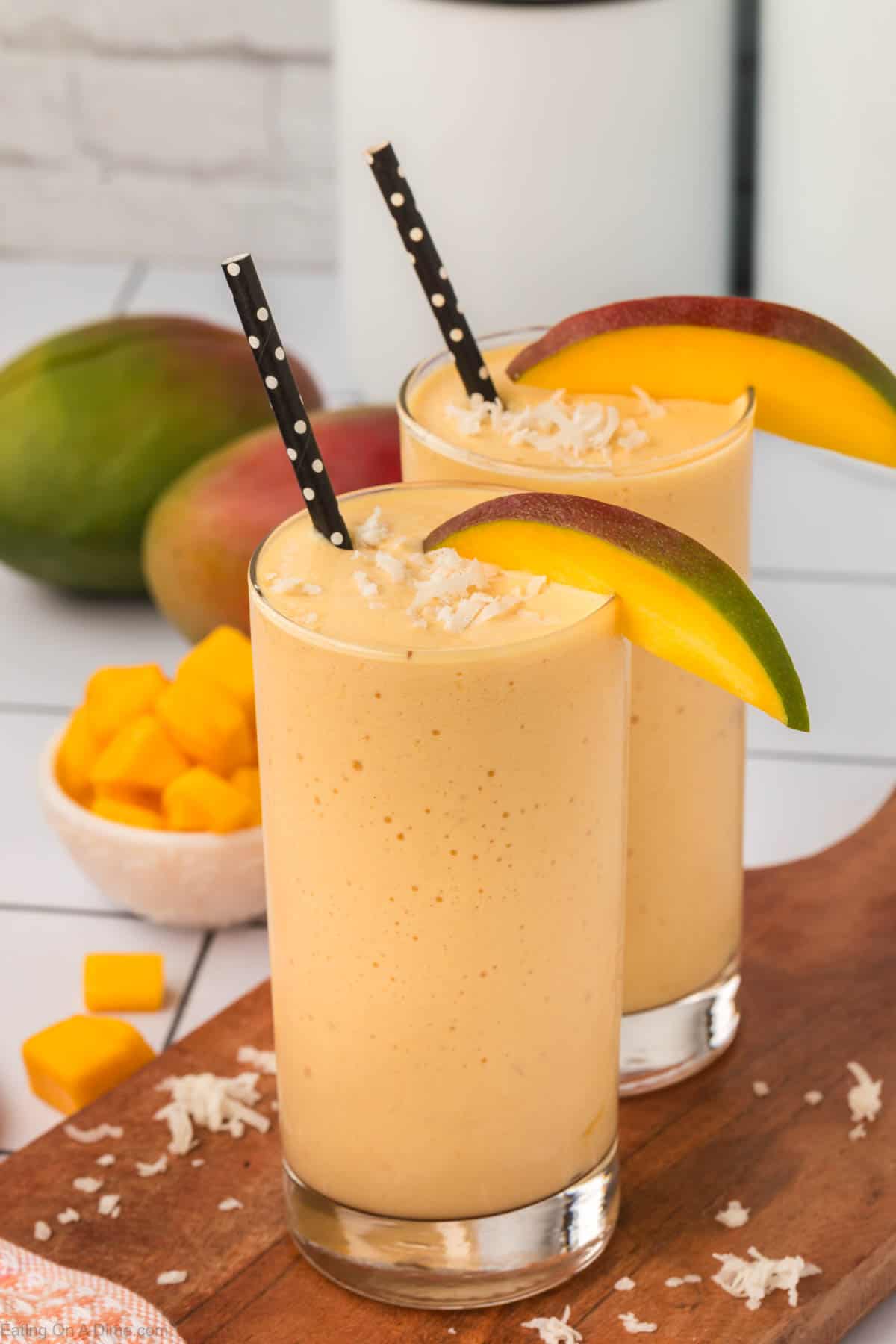 Mango Smoothie in a glass with straw topped with shredded coconut and slice mangos