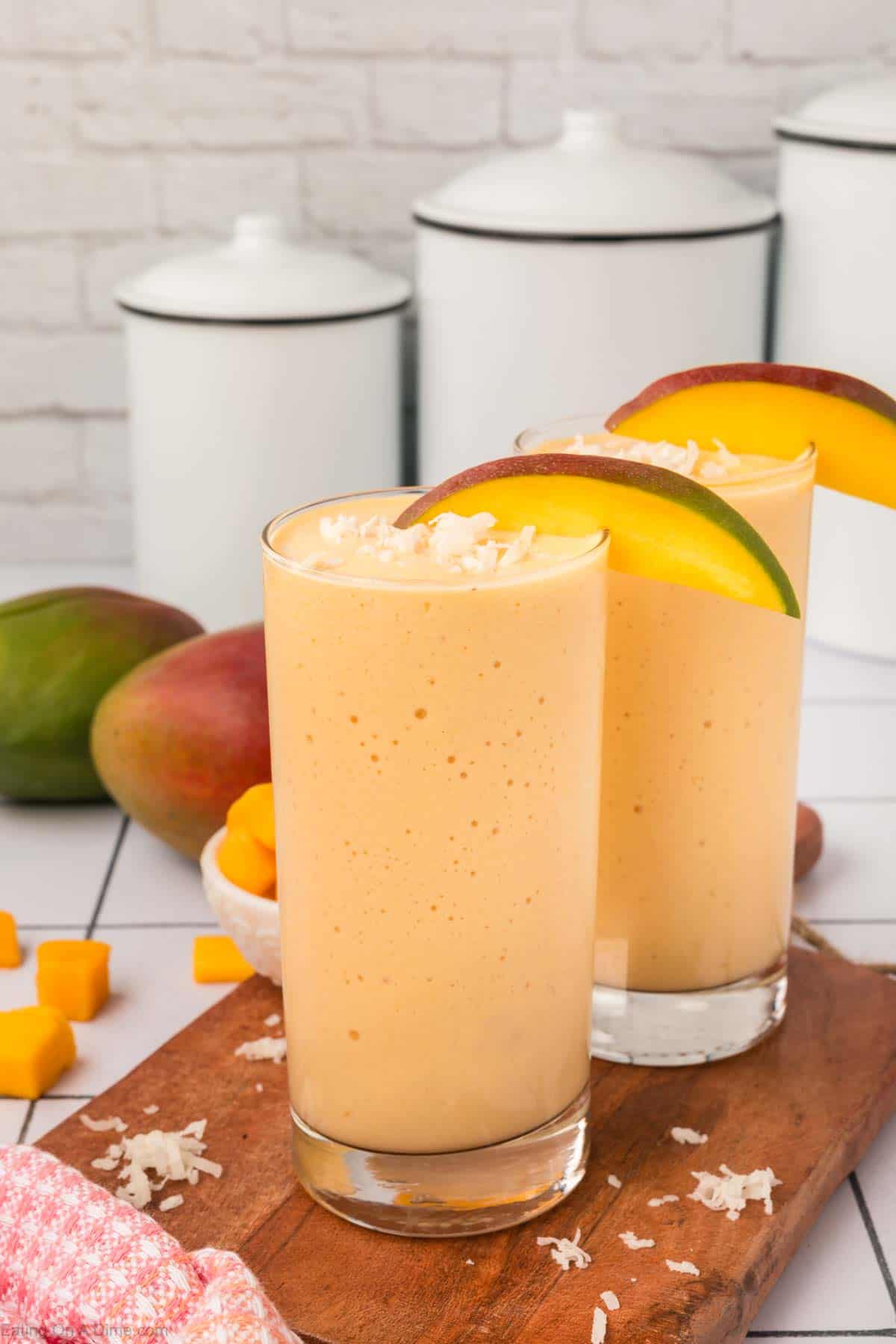 Mango Smoothie in a glass topped with shredded coconut and slice mangos