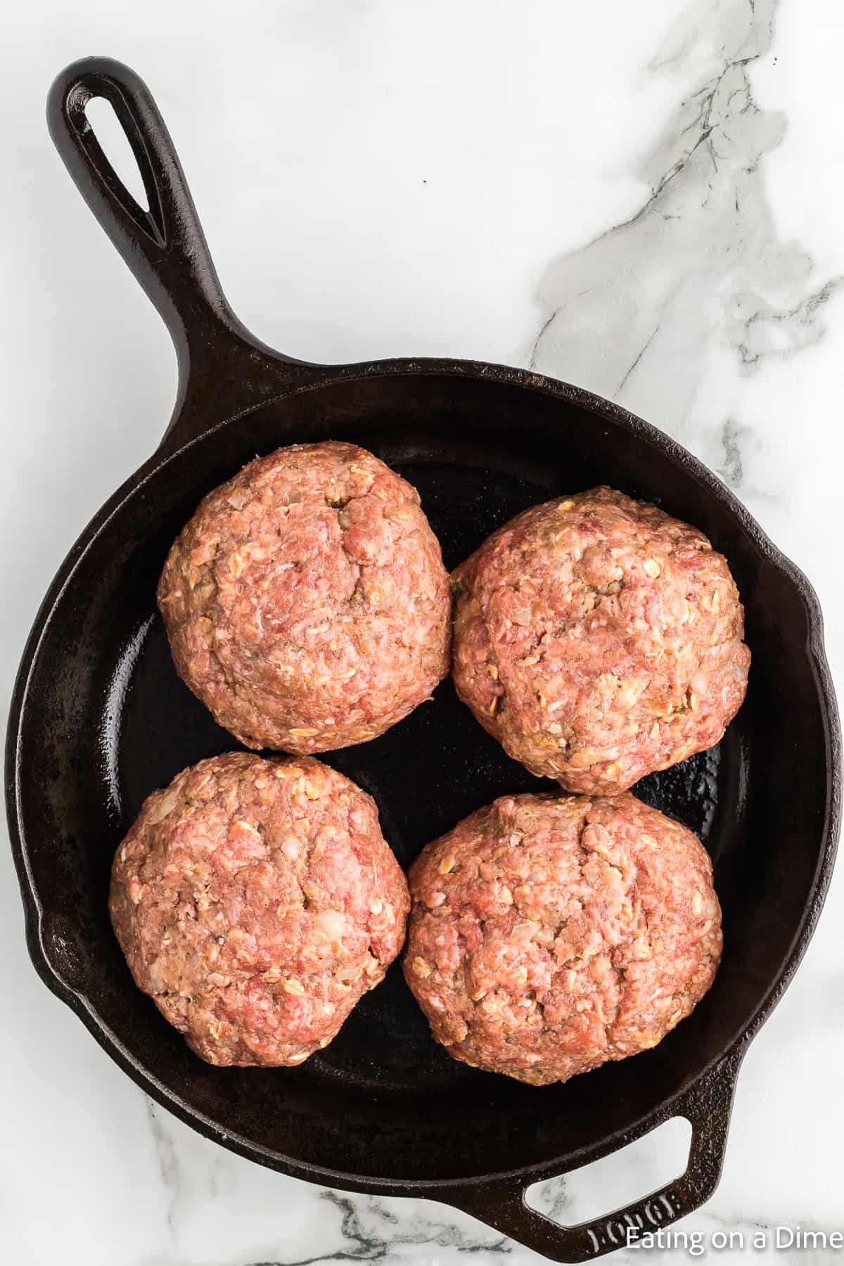 Placing ground beef patties in a cast iron skillet