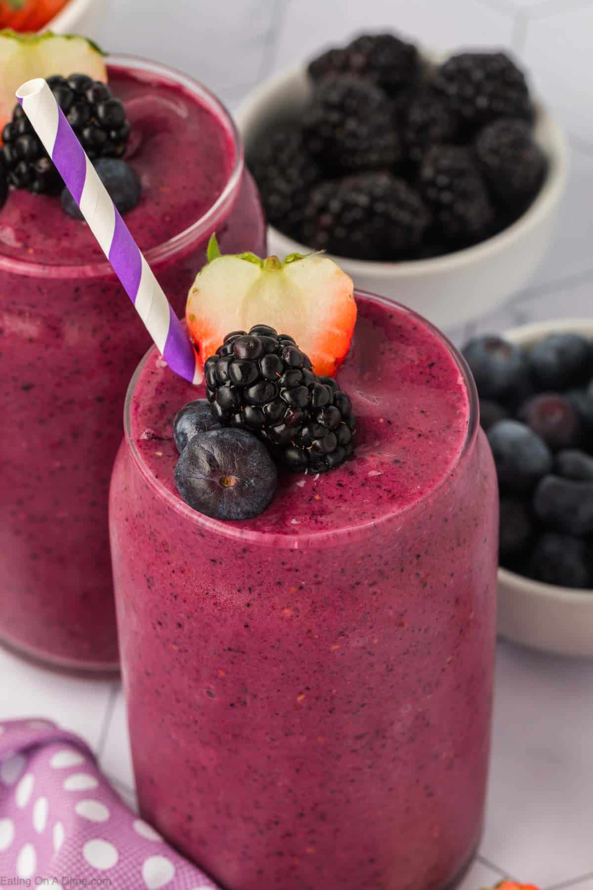 Mixed berry smoothie in a clear glass topped with blueberries, blackberries and slice strawberries