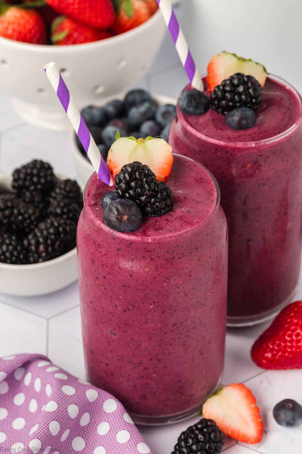 Mixed berries smoothie in a clear glass topped with blackberries, blueberries, and slice strawberries