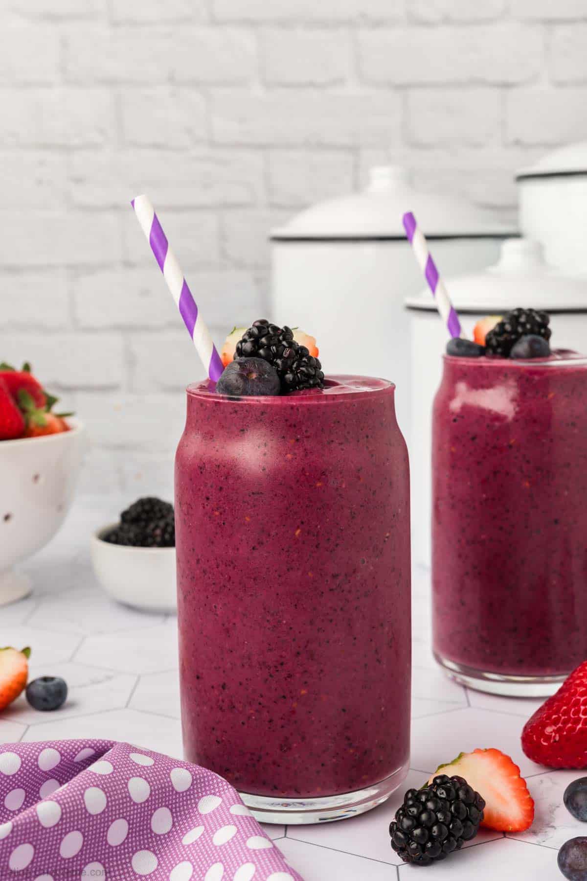 Mixed berries smoothie in a clear glass topped with blackberries, blueberries, and slice strawberries