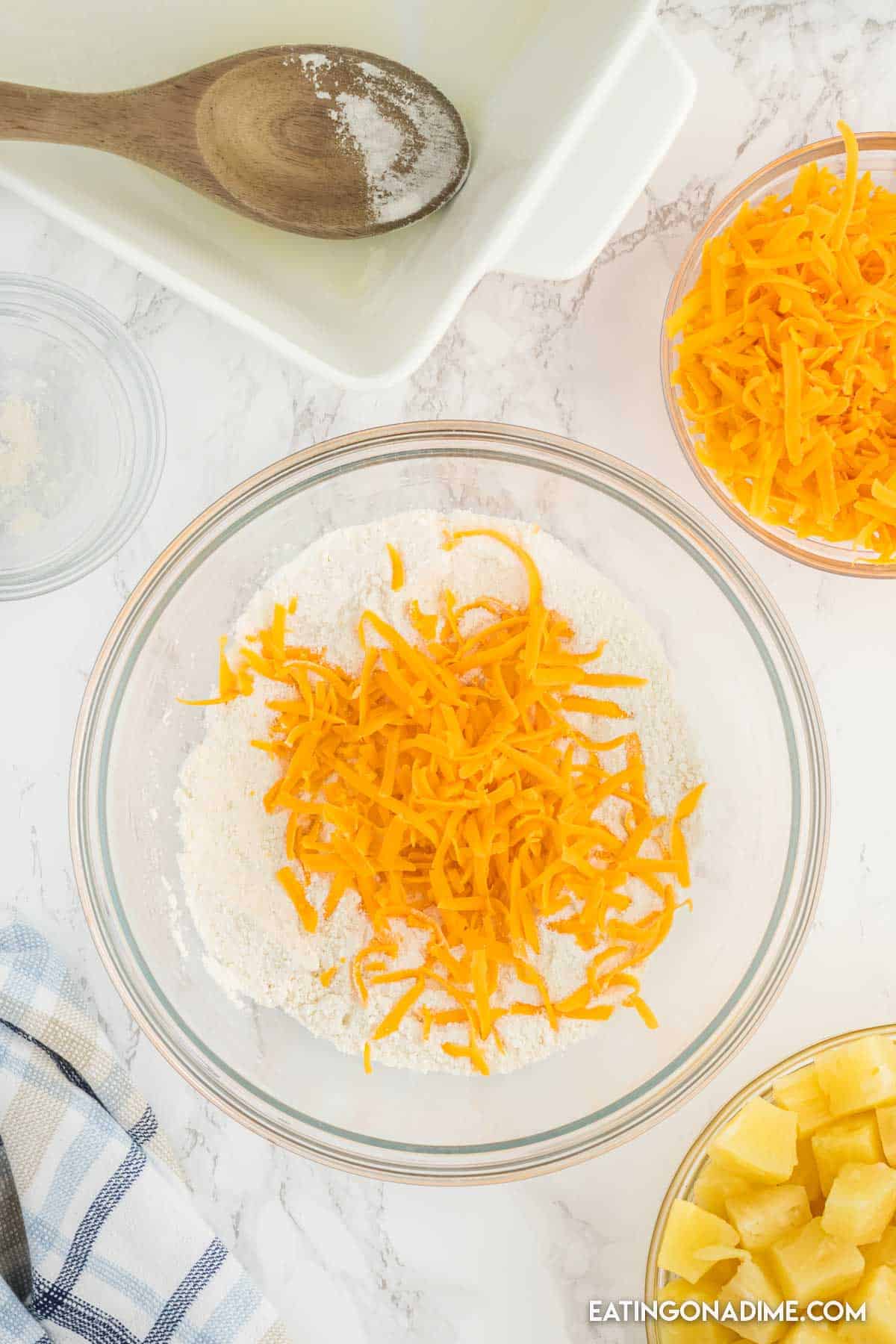 Combining flour and sugar with the shredded cheese in a bowl