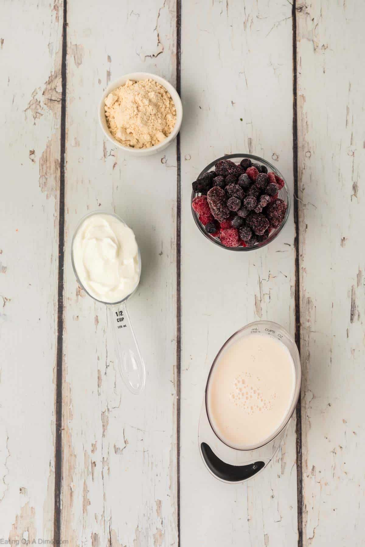 frozen mixed berries, a bowl of protein powder, yogurt, and milk